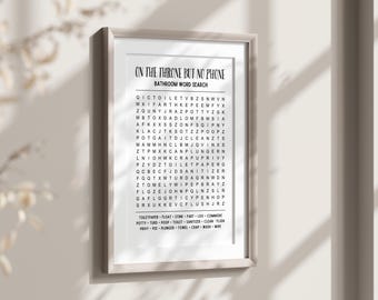 Könnte beinhalten: Gerahmter Badezimmer-Wortsuch-Kunstdruck mit dem Text "ON THE THRONE BUT NO PHONE". Der schwarze Text befindet sich auf weißem Hintergrund, und der Rahmen ist hellgrau. Der Druck enthält ein Wortsuchrätsel und eine Wortliste.