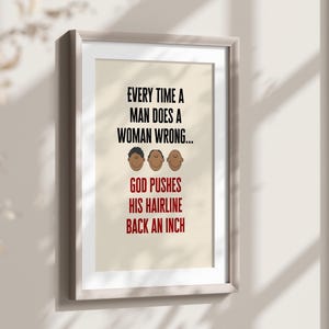 Puede incluir: Impresión enmarcada con el texto: "EVERY TIME A MAN DOES A WOMAN WRONG... GOD PUSHES HIS HAIRLINE BACK AN INCH." La impresión presenta tres caras de dibujos animados y está en un marco claro. El texto es en negro y rojo.