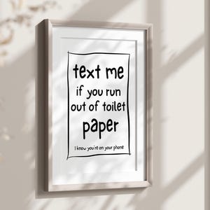 May include: Framed print with the text "text me if you run out of toilet paper. I know you're on your phone." The black text is inside a black outlined rectangle on a white background. The frame is a light gray color.