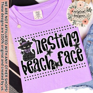 Op de afbeelding: Lichtpaars T-shirt met de zwarte tekst "resting beach face", versierd met zwarte sterren en stippen. Een cartoon zwarte kat met een heksenhoed staat links. Met Comfort Colors label.