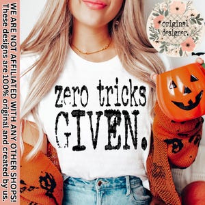 Puede incluir: Camiseta blanca con la frase "zero tricks GIVEN" en negro. La imagen incluye un recipiente naranja con forma de calabaza y un diseño floral con las palabras "original designer."