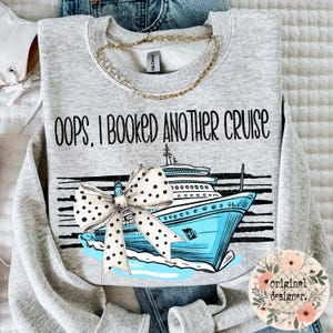 May include: A light gray crewneck sweatshirt featuring the black text OOPS, I BOOKED ANOTHER CRUISE above a graphic of a blue cruise ship with a large white bow with black polka dots layered over the front, set against horizontal black lines.
