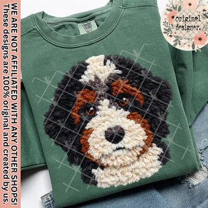 Può includere: Una felpa verde con un design testurizzato del muso di un cane Bernedoodle in nero, marrone e crema. Il muso del cane è al centro. La felpa ha un'etichetta Comfort Colors e un logo floreale "original designer".