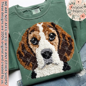 Puede incluir: Una sudadera verde con una imagen detallada y texturizada de la cara de un beagle. El pelaje del perro es marrón, blanco y negro, con ojos grandes y expresivos. La sudadera tiene cuello redondo y una etiqueta que dice "Comfort Colors".