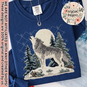 May include: A navy blue sweatshirt featuring an embroidered design of a howling wolf in front of a full moon and evergreen trees. The text "WE ARE NOT AFFILIATED WITH ANY OTHER SHOPS! These designs are 100% original and created by us." is printed on the left side.