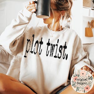 May include: A white sweatshirt with the text "plot twist" printed in black on the front. The sweatshirt is being worn by a person, but the person's face is not visible.