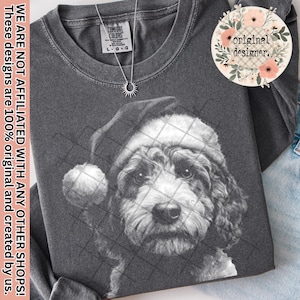 Op de afbeelding: Donkergrijze Comfort Colors sweatshirt met een zwart-wit illustratie van een hond met een kerstmuts. Een zilveren ketting met een zonnehanger is zichtbaar. De tekst "WE ARE NOT AFFILIATED WITH ANY OTHER SHOPS! These designs are 100% original and created by us." is gedrukt.