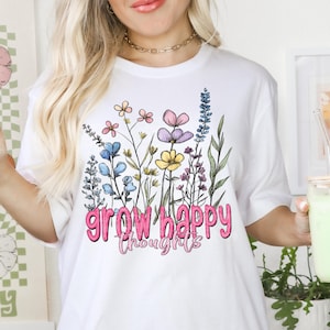 May include: White t-shirt featuring a floral design and the text "grow happy thoughts" in pink.