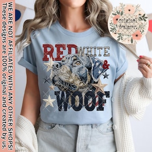 May include: Light blue t-shirt featuring a Rottweiler dog design with the words "RED WHITE & WOOF" in red, white, and blue. The design includes stars and a plaid pattern. The shirt also has the text "WE ARE NOT AFFILIATED WITH ANY OTHER SHOPS! These designs are 100% original and created by us."