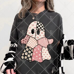 Pode incluir: Uma t-shirt cinzento-carvão de manga curta com um grande gráfico de fantasma composto por vários padrões de patchwork, incluindo laços cor-de-rosa, xadrez preto e branco, estampado de leopardo, bolinhas, riscas, margaridas, estrelas e corações.