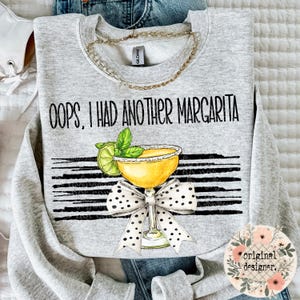 Könnte beinhalten: Grauer Sweatshirt mit dem Text "Oops, I had another margarita" in Schwarz. Auf dem Sweatshirt ist ein Margarita-Glas mit einem Limettenstück und einer Schleife abgebildet.