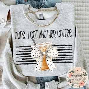May include: A light gray sweatshirt with the text "OOPS, I GOT ANOTHER COFFEE" above a graphic of an iced coffee with a polka dot bow. The design includes black and white horizontal stripes.