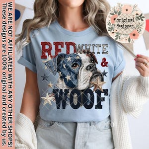 May include: Light blue t-shirt featuring a Boxer dog with a patriotic design. The dog's head is adorned with a denim-like pattern of stars and stripes. The shirt also displays the words "RED, WHITE & WOOF".