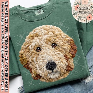 May include: A green sweatshirt with a detailed, textured image of a dog's face. The dog's fur is a mix of tan, brown, and cream colours. The sweatshirt has the text "COMFORT COLORS" on the tag. The text "WE ARE NOT AFFILIATED WITH ANY OTHER SHOPS! These designs are 100% original and created by us." is also visible.