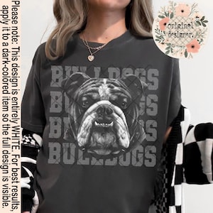 May include: Dark gray t-shirt featuring a grayscale bulldog graphic with the word "BULLDOGS" repeated vertically. The shirt has short sleeves and a crew neck. The text "original designer" is in a floral design.