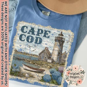 Op de afbeelding: Lichtblauw T-shirt met een Cape Cod-ontwerp met een vuurtoren, boot en kustlandschap. Het shirt bevat de tekst "CAPE COD" en de zin "WE ARE NOT AFFILIATED WITH ANY OTHER SHOPS! These designs are 100% original and created by us."