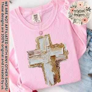 Könnte beinhalten: Ein hellrosa Langarmshirt mit einem strukturierten Kreuzdesign in Gold, Weiß und Beige. Das Shirt hat ein Comfort Colors-Etikett und eine kleine Anhängerkette. Auf dem Shirt steht "WE ARE NOT AFFILIATED WITH ANY OTHER SHOPS! These designs are 100% original and created by us."