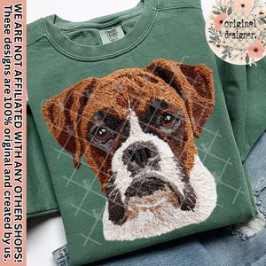 May include: A green sweatshirt with an embroidered Boxer dog design. The dog's fur is brown and white, with a detailed facial expression. The sweatshirt has the text "COMFORT COLORS" and "original designer."