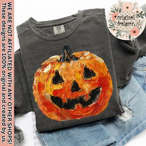 May include: A dark gray sweatshirt featuring a vibrant, textured pumpkin graphic in shades of orange, yellow, and black. The pumpkin has a carved face. The sweatshirt is folded over denim shorts. Text on the image reads: "WE ARE NOT AFFILIATED WITH ANY OTHER SHOPS! These designs are 100% original and created by us."