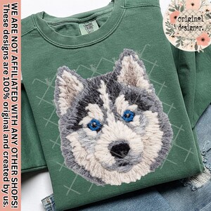 May include: Green sweatshirt with an embroidered husky face, showcasing blue eyes and gray and white fur. The design is on a Comfort Colors sweatshirt. The text on the side says "WE ARE NOT AFFILIATED WITH ANY OTHER SHOPS! These designs are 100% original and created by us."
