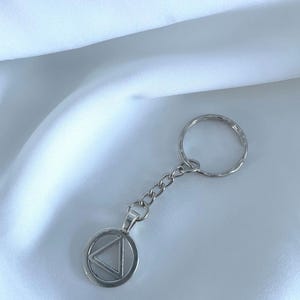 May include: Silver keyring with a circular charm featuring a triangle inside. The keyring is on a white background.
