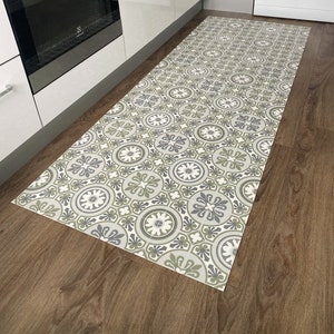 May include: A patterned kitchen rug with a geometric design in shades of grey, green, and white. The rug is placed on a wooden floor in a kitchen.