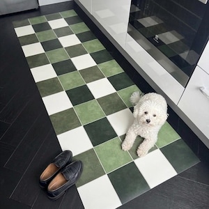 May include: A rectangular kitchen mat with a checkerboard pattern in shades of green and white. Black leather loafers are placed near the mat. A small white dog is lying on the mat.