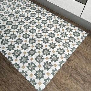 May include: A white, gray, and beige patterned kitchen rug with a geometric design. The rug is placed on a wood floor in front of a white cabinet.