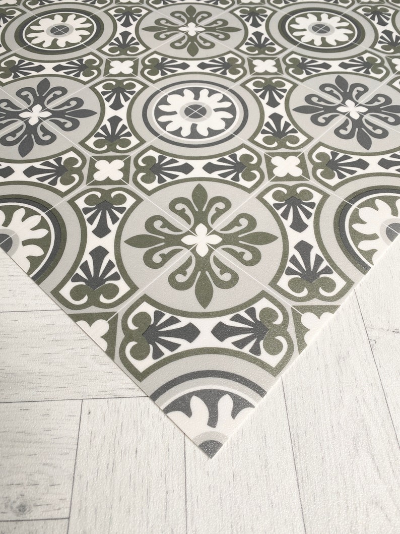 May include: A patterned floor tile with a repeating design of black, white, and grey floral motifs. The tile has a textured surface and a slightly raised edge.