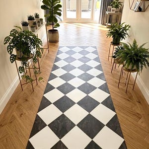 May include: A rectangular runner rug featuring a repeating diamond pattern in alternating solid white and dark gray marble-textured squares. The rug is positioned centrally on a light brown wooden floor with a herringbone pattern in a bright room.