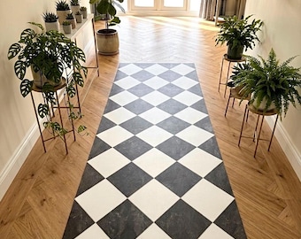 Puede incluir: Una alfombra rectangular tipo pasillero con un patrón de rombos que alterna cuadrados blancos sólidos y cuadrados gris oscuro con textura de mármol. La alfombra está colocada en el centro de un suelo de madera clara con patrón de espiga.