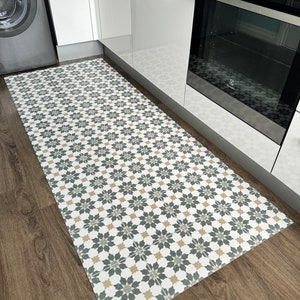 May include: A white, gray, and beige patterned kitchen rug with a geometric design. The rug is placed on a wood floor in a kitchen.