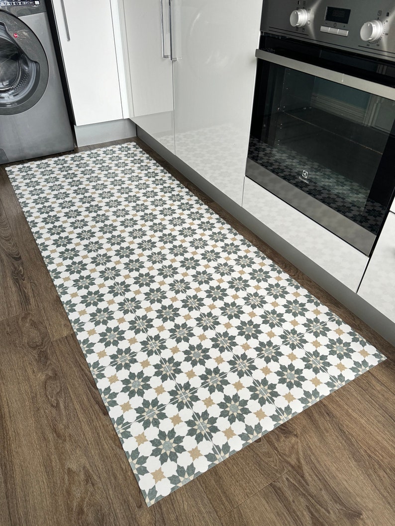 May include: A white, gray, and beige patterned kitchen rug with a geometric design. The rug is placed on a wood floor in a kitchen.
