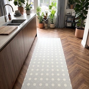 Puede incluir: Una alfombra de suelo larga y rectangular con un fondo gris claro y un patr&oacute;n geom&eacute;trico blanco repetitivo de l&iacute;neas finas que se cruzan y peque&ntilde;as formas de estrellas florales, colocada sobre un suelo de madera en una cocina.