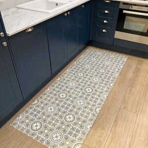 May include: A patterned kitchen rug with a geometric design in shades of grey and green on a white background. The rug is placed in front of a kitchen sink and cabinets.