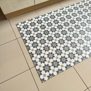 May include: A patterned kitchen rug with a geometric design in shades of white, black, and beige. The rug is made of a durable material and is perfect for protecting floors from spills and stains.