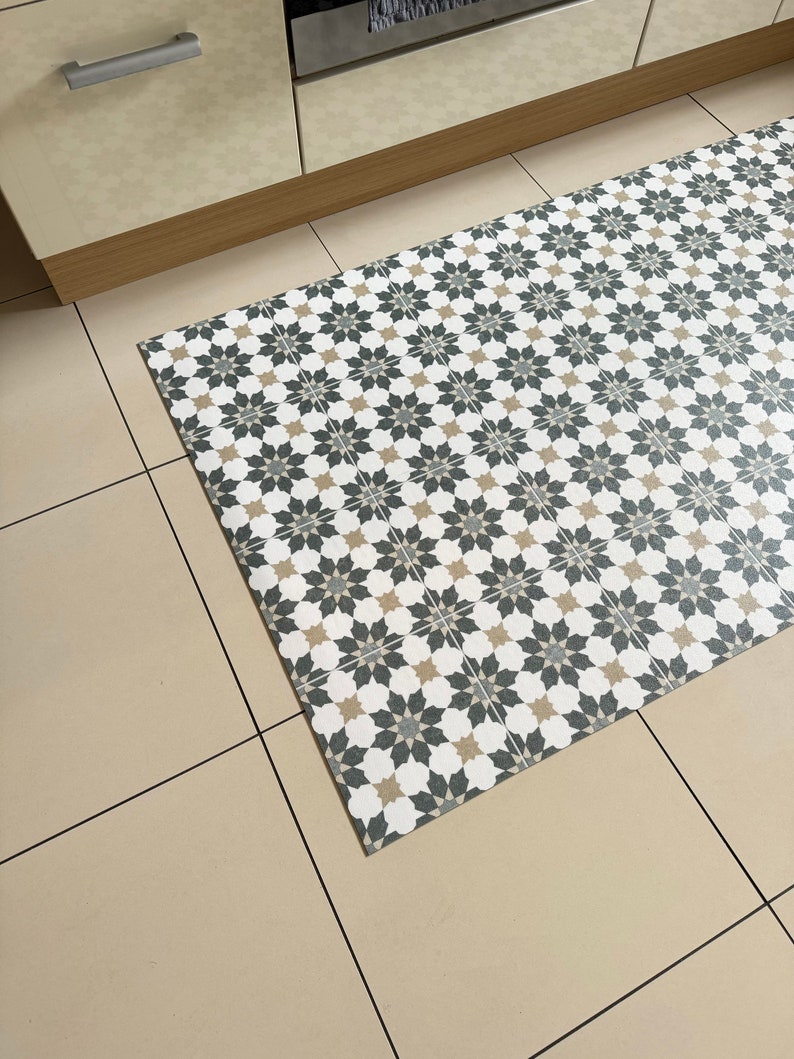 May include: A patterned kitchen rug with a geometric design in shades of white, black, and beige. The rug is made of a durable material and is perfect for protecting floors from spills and stains.