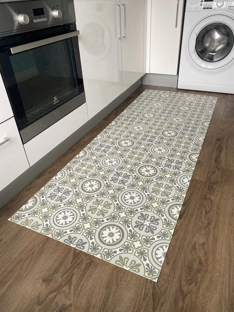 May include: A patterned kitchen rug with a geometric design in shades of grey, green, and white. The rug is placed on a wooden floor in a kitchen.