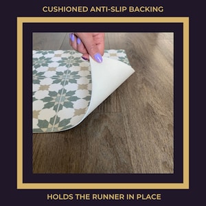 May include: Close-up of a green and beige patterned rug with a white, cushioned anti-slip backing. The backing is visible as the rug is being lifted up. "CUSHIONED ANTI-SLIP BACKING" and "HOLDS THE RUNNER IN PLACE" are written in black text on a gold background.