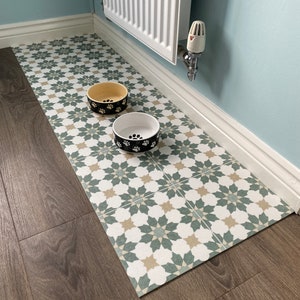 May include: A green and white patterned floor mat with two dog bowls, one yellow and one black, on top of it. The bowls are both decorated with paw prints.