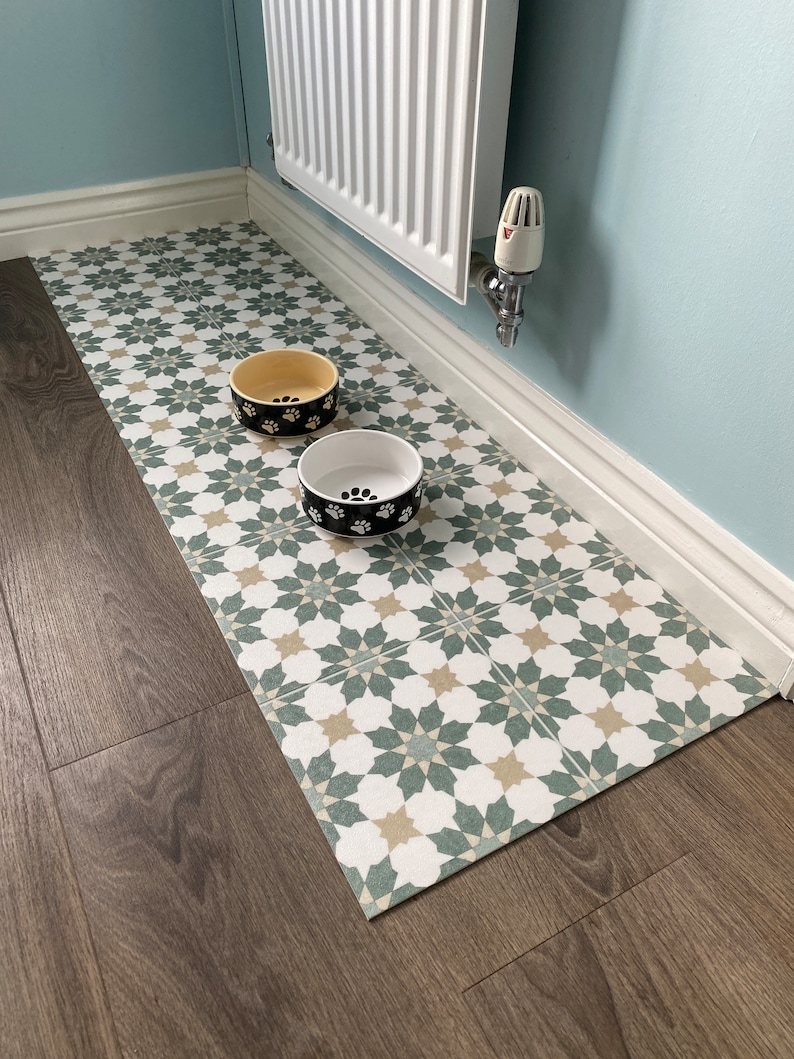 May include: A green and white patterned floor mat with two dog bowls, one yellow and one black, on top of it. The bowls are both decorated with paw prints.