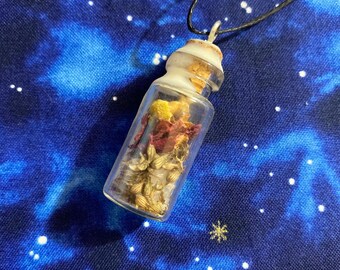 Puede incluir: Una pequeña botella de vidrio llena de flores y hierbas secas cuelga de un cordón negro. La botella tiene un tapón de corcho y está llena de flores y hierbas secas en tonos amarillos, rojos y blancos. La botella cuelga sobre un fondo azul con estrellas blancas.