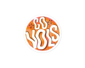 Könnte beinhalten: Ein runder Aufkleber mit einem orange-rosa Wirbelmuster. Der Aufkleber sagt "Go Vols" in weißen Buchstaben mit schwarzem Umriss.