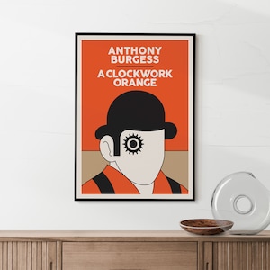 May include: A black and white poster with an orange background. The poster features a minimalist illustration of a man wearing a bowler hat and a single eye with a gear in it. The text on the poster reads "Anthony Burgess, A Clockwork Orange."