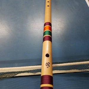Puede incluir: Una flauta de madera con un adorno decorativo marrón, naranja, verde y morado. La flauta tiene seis agujeros para los dedos y un solo agujero de soplado. La flauta está marcada con el número "42".