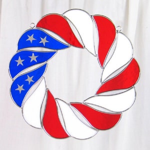 May include: A stained glass wreath in the shape of a circle, with red, white, and blue glass pieces arranged in a spiral pattern. The blue pieces have white stars on them, resembling the American flag.