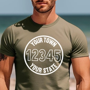 Peut inclure: Un t-shirt vert avec un motif circulaire blanc qui dit "YOUR TOWN 12345 YOUR STATE".