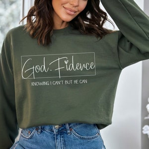 以下が含まれることがあります： 白い文字で「God. Fidence」と「Knowing I can't but He can」と書かれた緑色のスウェットシャツです。