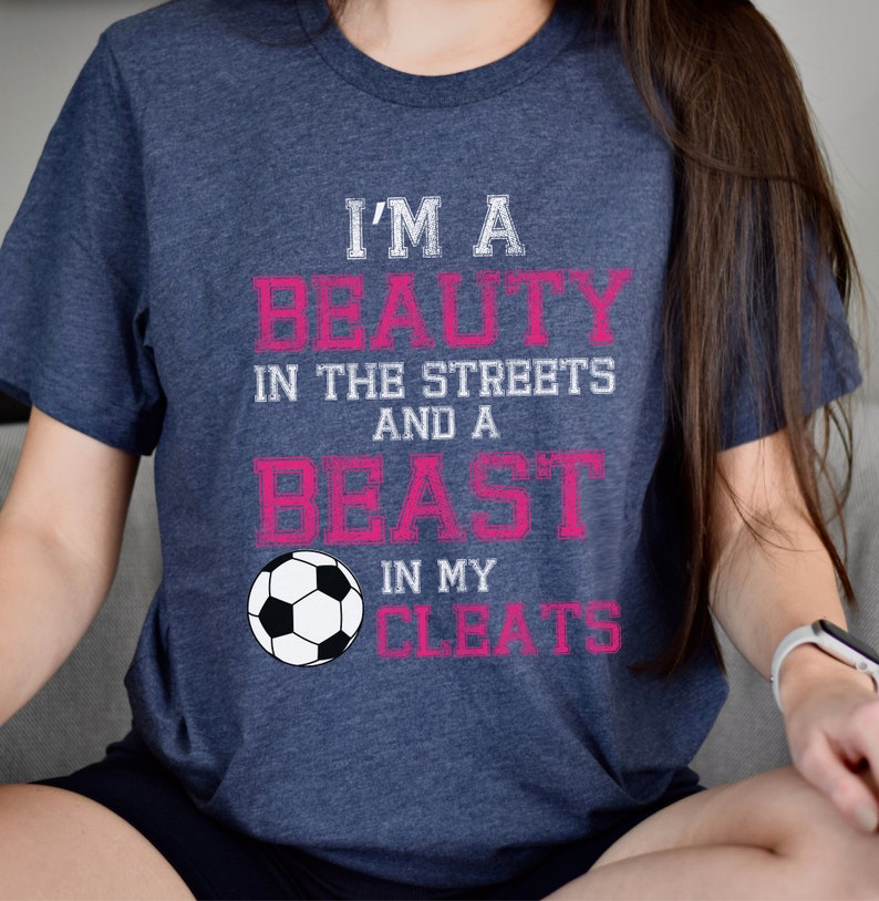 May include: A navy blue t-shirt with the text "I'm a beauty in the streets and a beast in my cleats" in pink and white lettering. A white soccer ball is centered below the text.