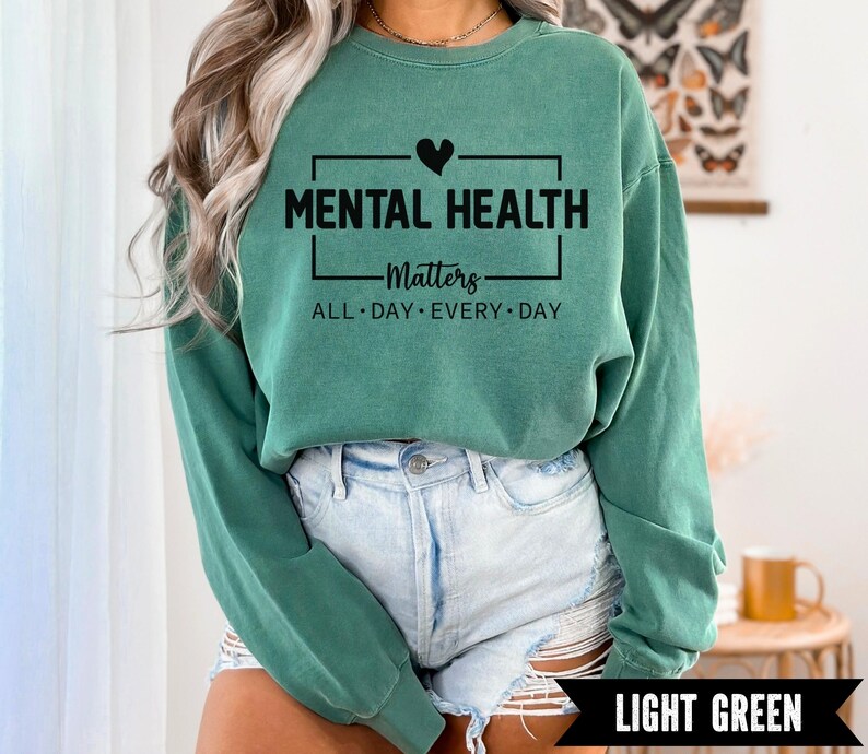 Peut inclure: Sweat-shirt vert clair avec le texte "MENTAL HEALTH Matters ALL DAY EVERY DAY" en noir. Le motif comprend un c&oelig;ur noir au-dessus du mot "MENTAL HEALTH". Le sweat-shirt est associ&eacute; &agrave; un short en jean d&eacute;lav&eacute;.